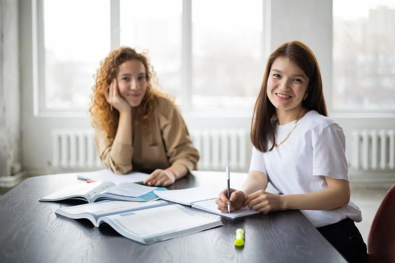 Two women smile while writing in notebooks their ideas about B2B content marketing