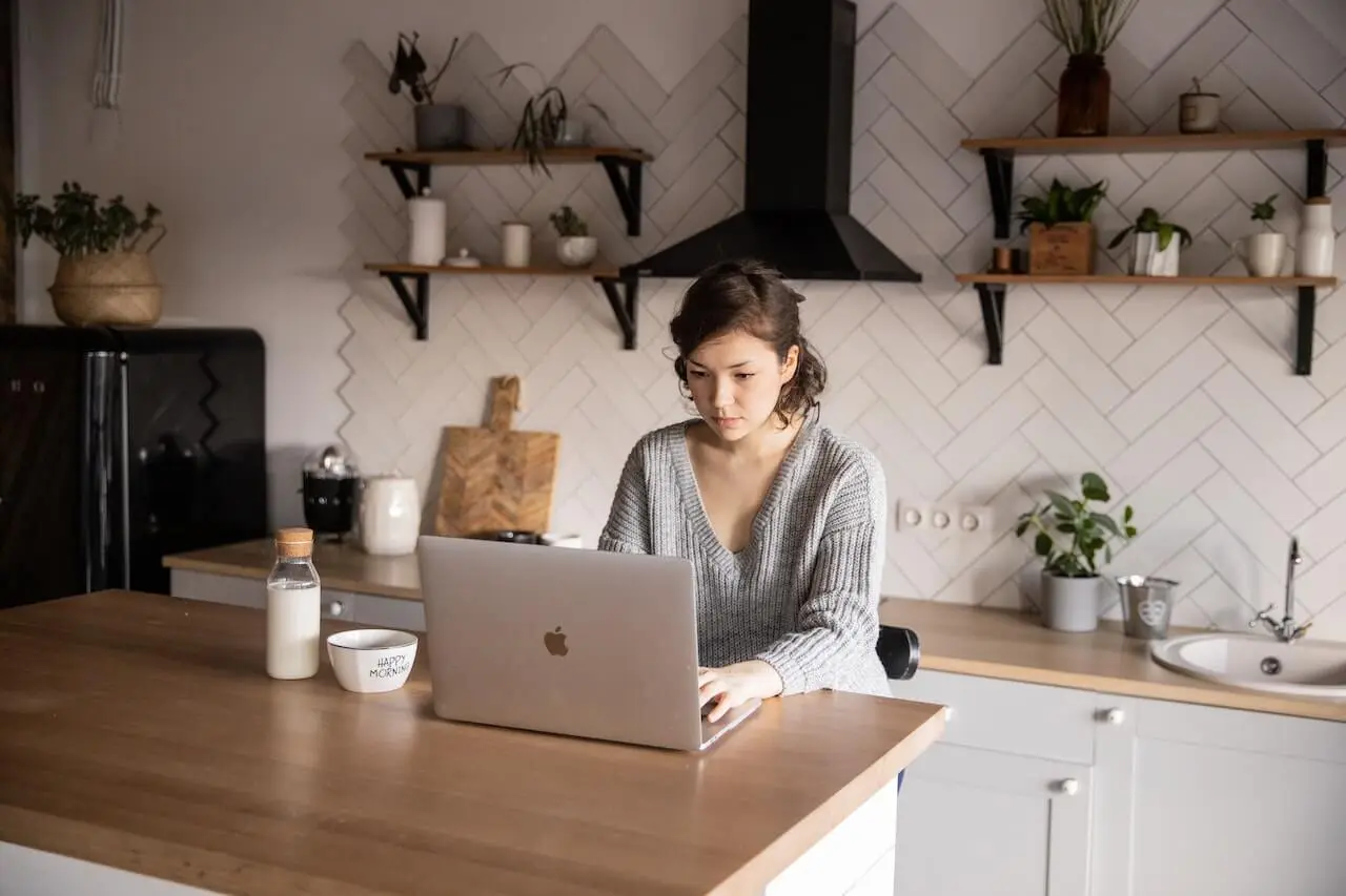 Content young woman browsing laptop in modern kitchen as an example of customer archetypes diversity.