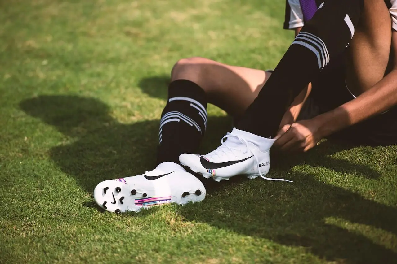 Athlete sitting on the grass wearing Nike football shoes. 