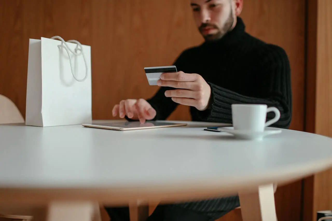 Young man looking at his credit card while making an online purchase.