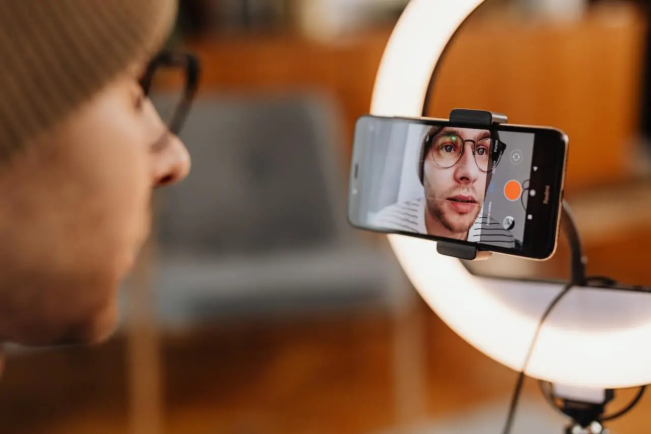 A man films a video with a smartphone and ring light, creating a user generate content.