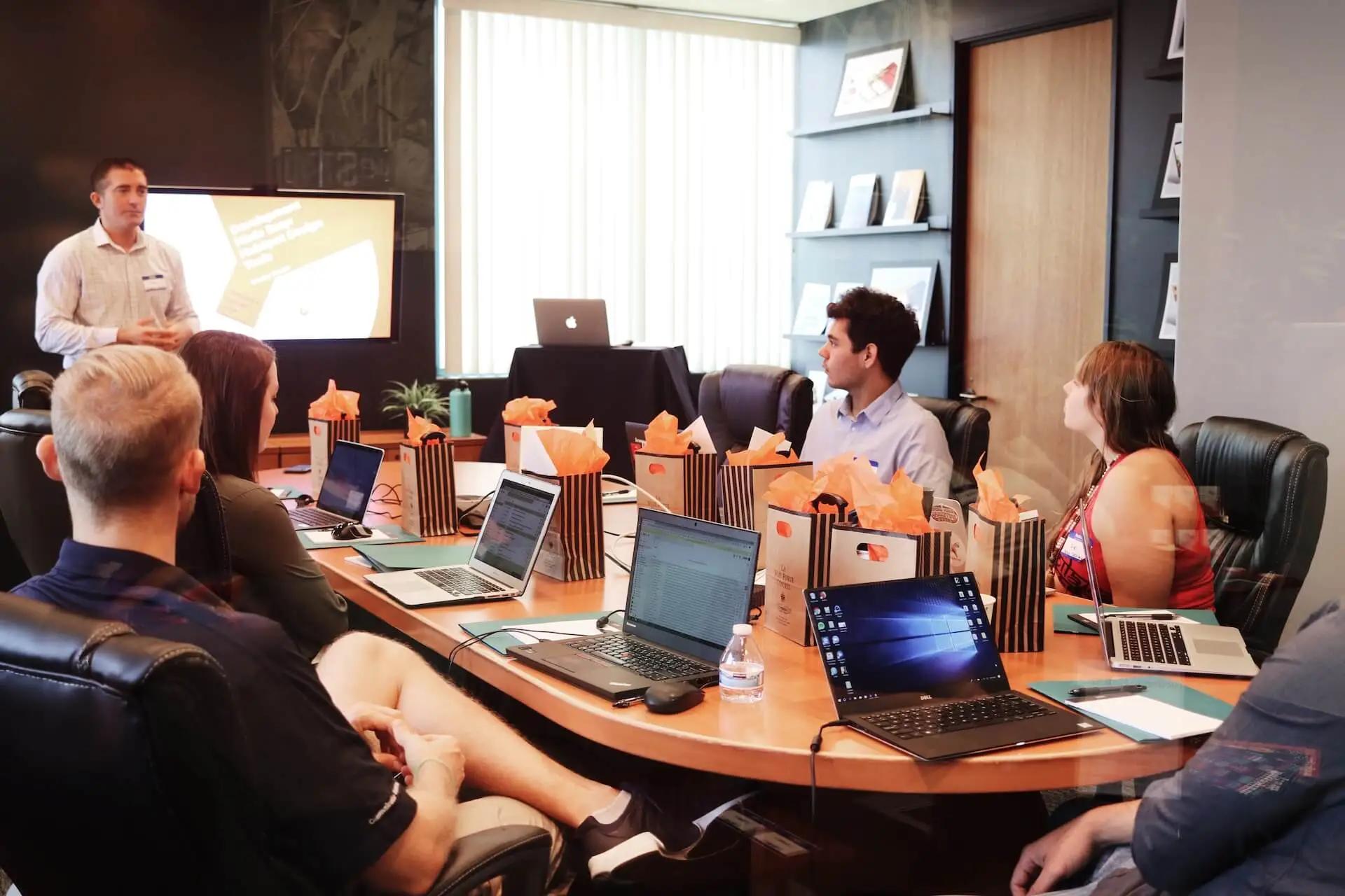 A meeting room with team members with laptops while a fourth presents data.
