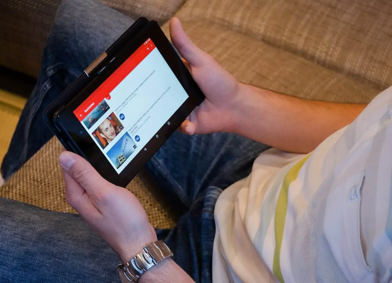 Image of a man sitting on a couch and holding a tablet with the YouTube app open.