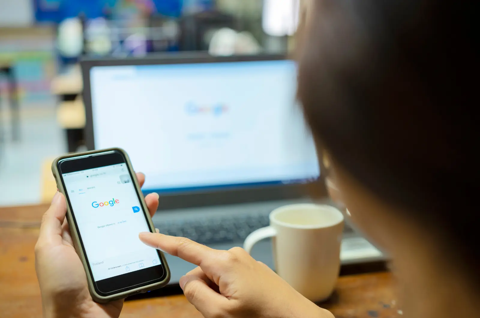 User searching Google on a smartphone with a laptop in the background