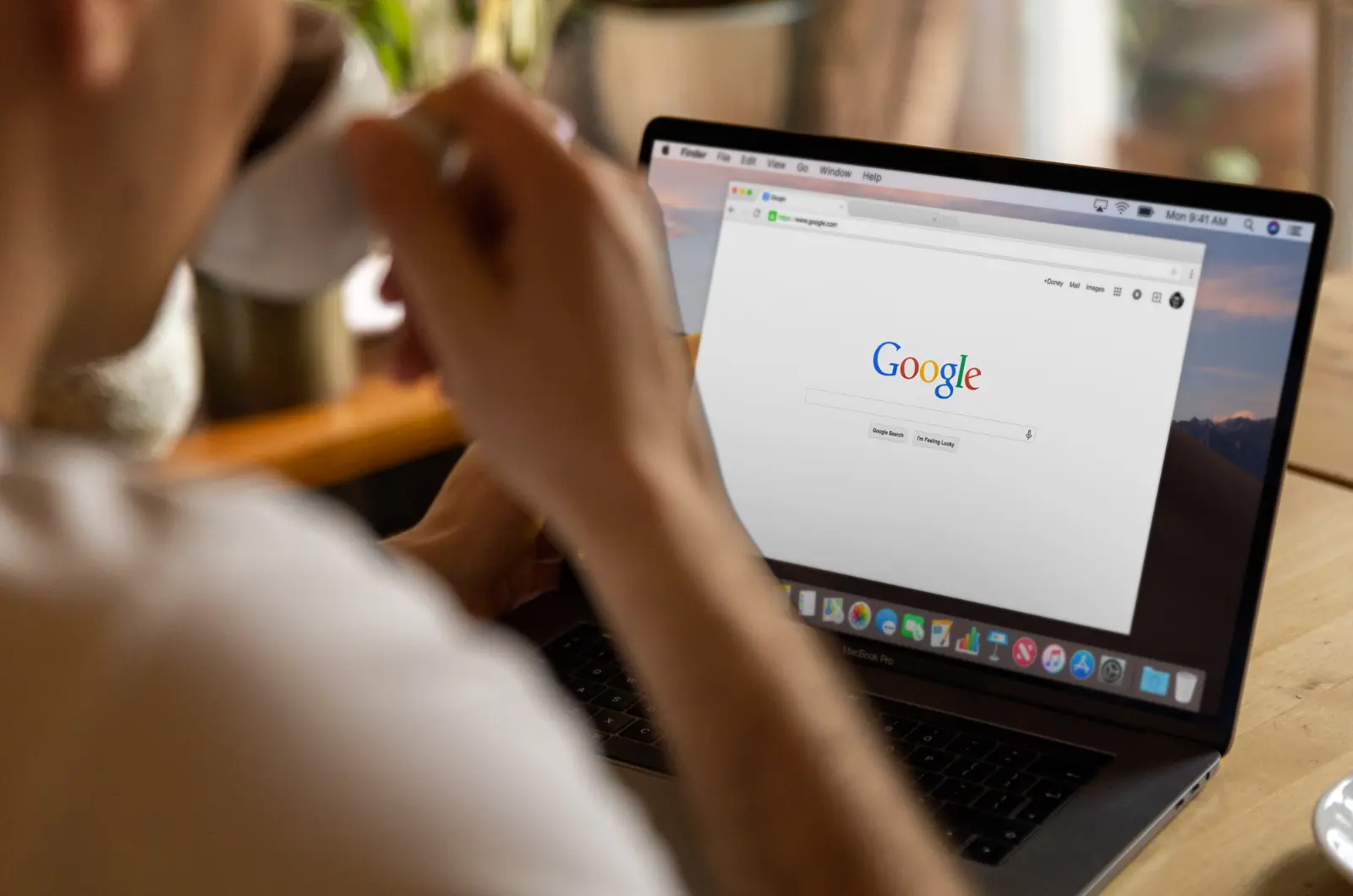 Person browsing Google search on laptop while holding coffee